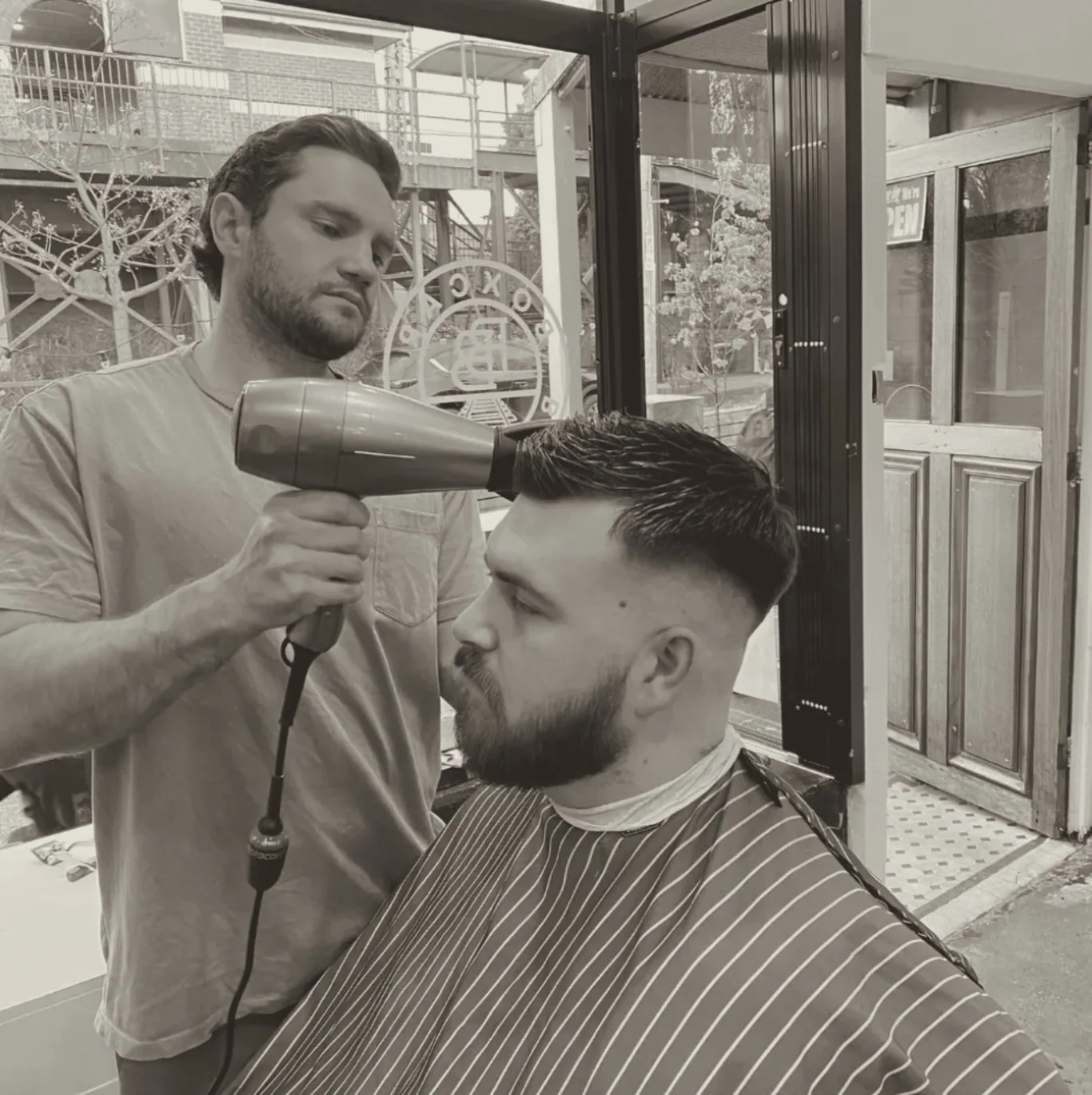 A Boxcar barber blow-drying and finishing a client's cut beside the front door