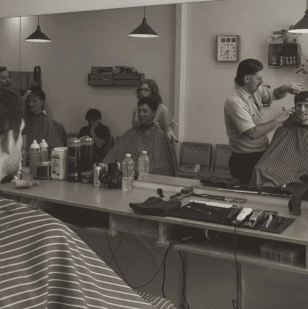 Inside Boxcar Barbers — two barbers working the mirror bench
